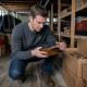Man crouching in a cluttered basement holding a small cigar box, looking intently inside.