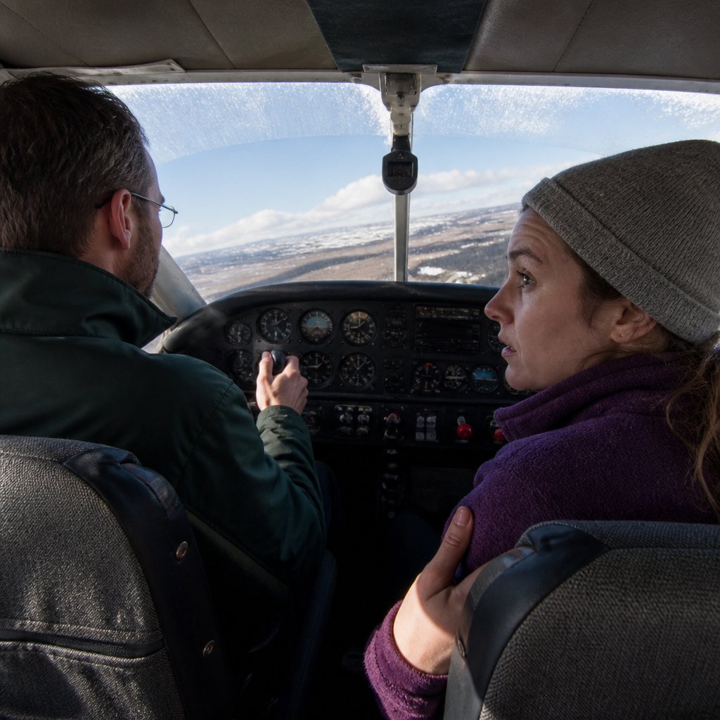 Man piloting small plane as tundra rushes up through cloud cover, woman tense beside him.